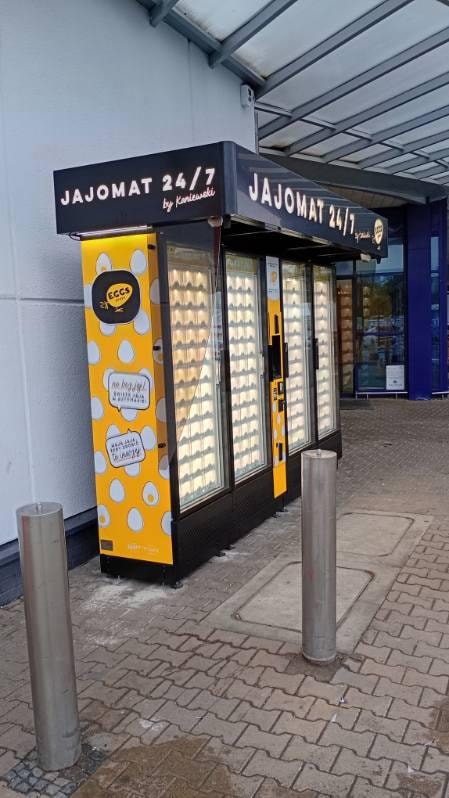 Side view of a yellow egg vending machine beside a shop